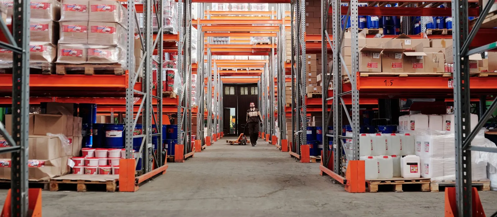 Warehouse aisle lined with orange and gray pallet racking holding wrapped pallet loads